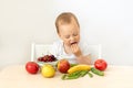 Baby boy 2 years old sitting at a table on a white isolated background and eating fruits vegetables, baby food concept, place for Royalty Free Stock Photo