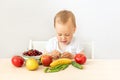 Baby boy 2 years old sitting at a table on a white isolated background and eating fruits vegetables, baby food concept, place for Royalty Free Stock Photo