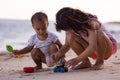 Baby boy and young girl sitting on sandy beach near the sea, playing with sand scoop and toy car. Brother and sister playing Royalty Free Stock Photo