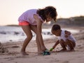 Baby boy and young girl sitting on sandy beach near the sea, playing with sand scoop and toy car. Brother and sister playing Royalty Free Stock Photo