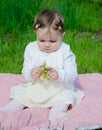 Baby in bright clothes on a pink plaid on green grass in the park