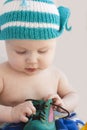 The baby in a cap plays with a green one shoe