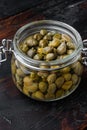 Baby capers in marinated glass jar, on dark wooden background