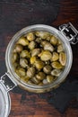 Baby capers in marinated glass jar, on dark wooden background, top view