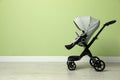 Baby carriage. Modern pram near light green wall, space for text