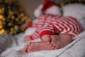 Baby in Christmas pajamas and Santa hat sleeping on bed indoors, focus on feet Royalty Free Stock Photo