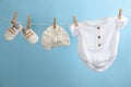 Baby clothes and accessories hanging on washing line against light blue background Royalty Free Stock Photo