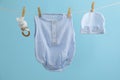 Baby clothes and accessories hanging on washing line against light blue background Royalty Free Stock Photo