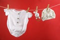 Baby clothes and accessories hanging on washing line against red Royalty Free Stock Photo