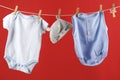 Baby clothes hanging on washing line against red background Royalty Free Stock Photo