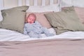 A baby in clothes sleeps on a large bed in the bedroom of adult parents