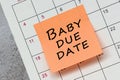 Baby due date written on a orange paper sticky note and stuck to a calendar. Royalty Free Stock Photo