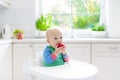 Baby boy eating apple in white kitchen at home Royalty Free Stock Photo