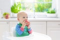 Baby boy eating apple in white kitchen at home Royalty Free Stock Photo