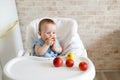 Baby eating fruit. Little girl biting yellow apple sitting in white high chair in sunny kitchen. Healthy nutrition for kids. Snack Royalty Free Stock Photo