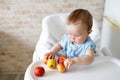 Baby eating fruit. Little girl biting yellow apple sitting in white high chair in sunny kitchen. Healthy nutrition for kids. Solid Royalty Free Stock Photo