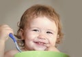 Baby eating. Portrait of funny little smiling boy with blonde curly hair and round cheecks eating from green plate