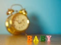 Baby. English alphabet made of wooden letter color. Alphabet baby on wooden table and vintage alarm clock and background is powder