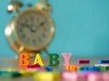 Baby. English alphabet made of wooden letter color. Alphabet baby on wooden table and vintage alarm clock and background is powder