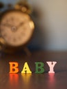 Baby. English alphabet made of wooden letter color. Alphabet baby on wooden table and vintage alarm clock