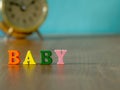 Baby. English alphabet made of wooden letter color. Alphabet baby on wooden table and vintage alarm clock and background is powder