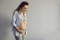 Portrait of happy young woman standing on gray background and touching her hands to her big belly. Royalty Free Stock Photo