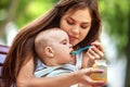 Baby feeding spoon by mother in park outdoor. Weaning .