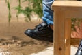 Baby feet of boy wears black leather shoes sitting on a wooden chair with copy space on the left Royalty Free Stock Photo