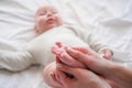 Baby feet in mother hands. Young caucasian woman makes massage for happy infant baby on white bed at home. Babycare Royalty Free Stock Photo