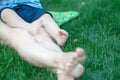 Baby feet on mother`s legs relaxing on green grass at summer day