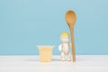 A baby figurine with a wooden spoon and a cup of banana dessert on a wooden table. The concept of healthy baby food