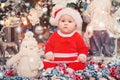 Baby first Christmas. New Year`s holidays. Baby with santa hat with gift. Living room decorated by Christmas tree and present gift Royalty Free Stock Photo