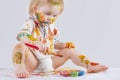 The baby is focused. The child messy paints his face and clothes with paint