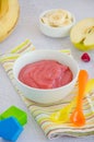 Baby food. Homemade apple puree or sauce with banana and raspberries in a bowl with a spoon on a light background. Healthy food. Royalty Free Stock Photo