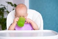 Baby food. little caucasian child drinks water from green plastic cup on highchair. Newborn infant kids Royalty Free Stock Photo