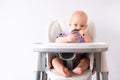 Baby food. little caucasian child drinks water from green plastic cup on highchair on white background. Newborn infant Royalty Free Stock Photo