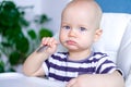 Baby food. little serious caucasian child with spoon in his mouth on highchair. Newborn infant kids