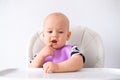 Baby food. little thoughtful caucasian baby girl in pink bib on highchair at home over white background. Newborn infant