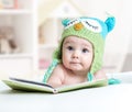 Baby in funny owl knitted hat owl lying with book in nursery Royalty Free Stock Photo