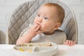 Excited baby girl touches food leftovers on plate and tastes