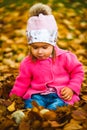 Baby girl in autumn park sitting in pile of dry leaves having fun. Autumn theme