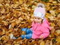 Baby girl in autumn park sitting in pile of dry leaves having fun. Autumn theme