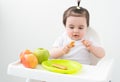 Baby girl in baby chair eating apples and cookies on white background. Baby first solid food