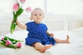 Baby girl in blue dress playing with bunch of pink tulips