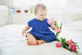 Baby girl in blue dress playing with bunch of pink tulips