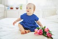 Baby girl in blue dress playing with bunch of pink tulips