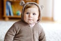 Baby girl with blue eyes wearing brown bear winter overal in sunny bedroom. Newborn child being dressed for an outdoor Royalty Free Stock Photo