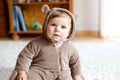 Baby girl with blue eyes wearing brown bear winter overal in sunny bedroom. Newborn child being dressed for an outdoor Royalty Free Stock Photo