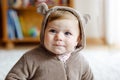 Baby girl with blue eyes wearing brown bear winter overal in sunny bedroom. Newborn child being dressed for an outdoor Royalty Free Stock Photo