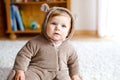 Baby girl with blue eyes wearing brown bear winter overal in sunny bedroom. Newborn child being dressed for an outdoor Royalty Free Stock Photo